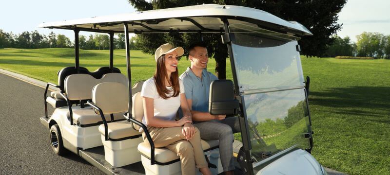 A man and a woman riding in a golf cart