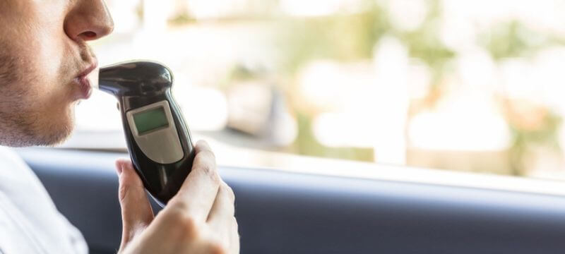 Man blowing into a breathalyzer in a car